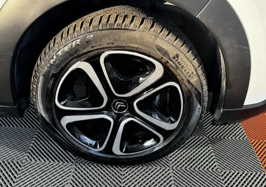 Gros plan sur la roue avant droite d'une Citroën C3 blanche, mettant en valeur la jante noire et argentée au design moderne.