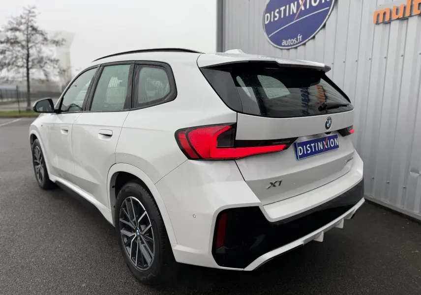 BMW X1 blanc minéral vue 3/4 arrière droit, avec feux arrière LED et jantes alliage noires contrastées.