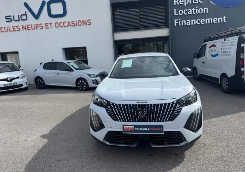Peugeot 2008 blanc vue de face, avec calandre noire distinctive et barres de toit visibles en arrière-plan.