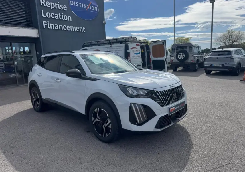 Vue 3/4 avant droit d’un Peugeot 2008 blanc 2024 avec barres de toit et jantes alliage noires.