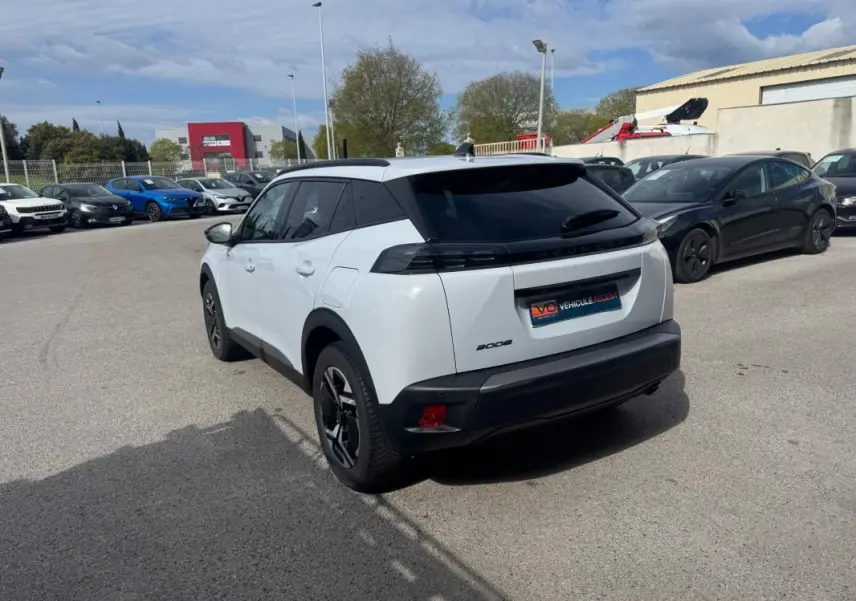 Peugeot 2008 blanc vue 3/4 arrière droit, avec barres de toit noires et jantes alliage 17 pouces.
