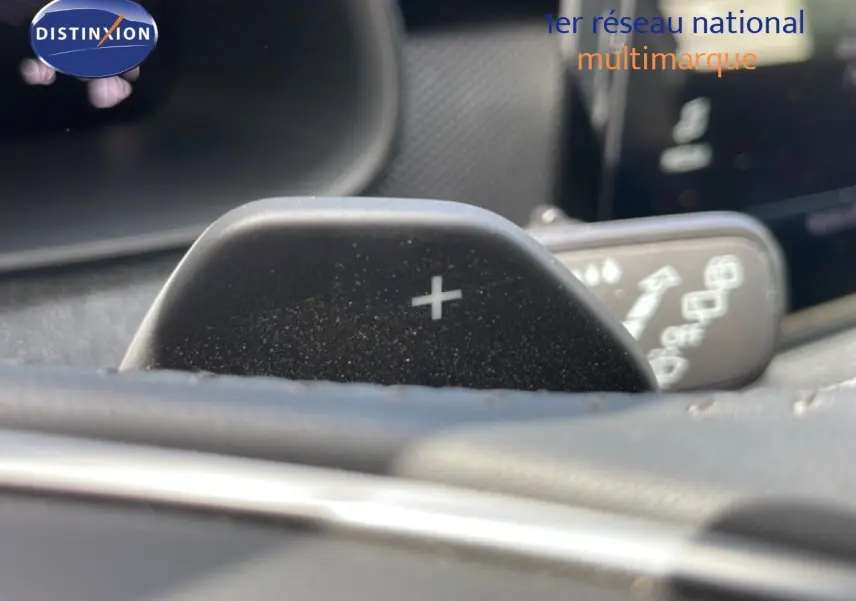 Gros plan sur la palette de changement de vitesse "+" du volant d'une Skoda Scala blanche Glacier, intérieur gris-noir.