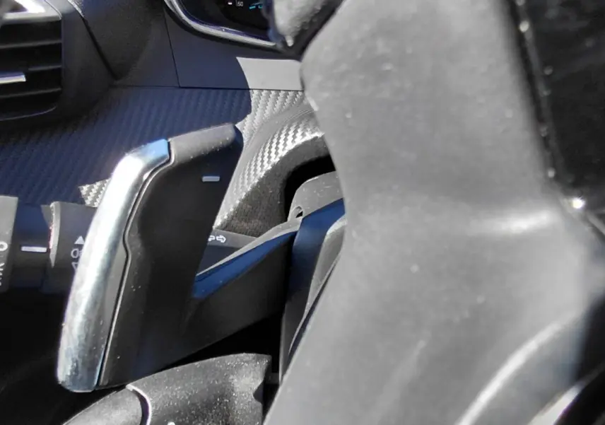 Gros plan sur la palette de changement de vitesse derrière le volant d’un Peugeot 2008 Hybrid bleu, intérieur noir.