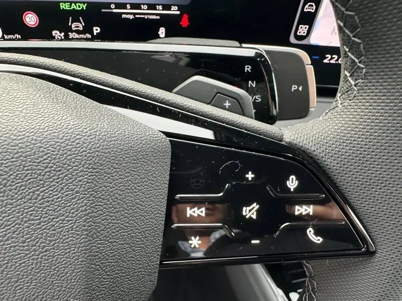 Gros plan sur les commandes tactiles du volant côté gauche de l'Audi Q3 2026 noir Mythique, avec affichage numérique en arrière-plan.