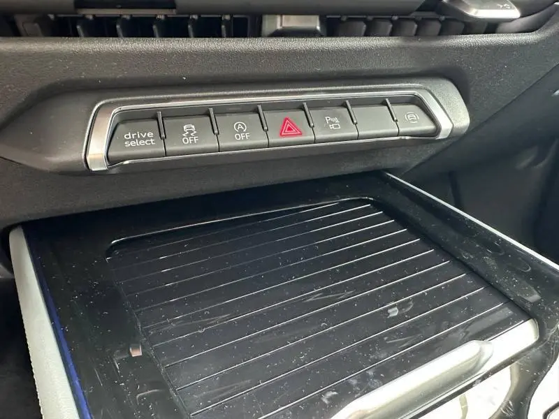 Gros plan sur la console centrale noire de l'Audi Q3 2026, avec rangée de boutons fonctionnels et surface de rangement striée.