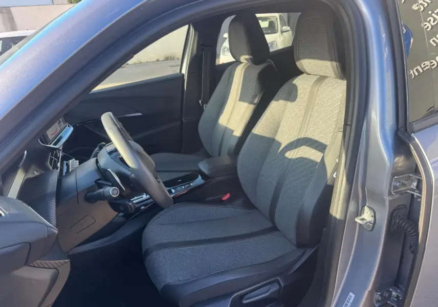 Vue intérieure côté conducteur du Peugeot 2008 Hybrid gris 2024, sièges tissu et tableau de bord moderne avec écran tactile.