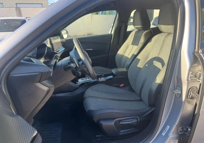 Intérieur avant droit du Peugeot 2008 Hybrid gris 2024, sièges tissu gris et tableau de bord moderne avec écran tactile.