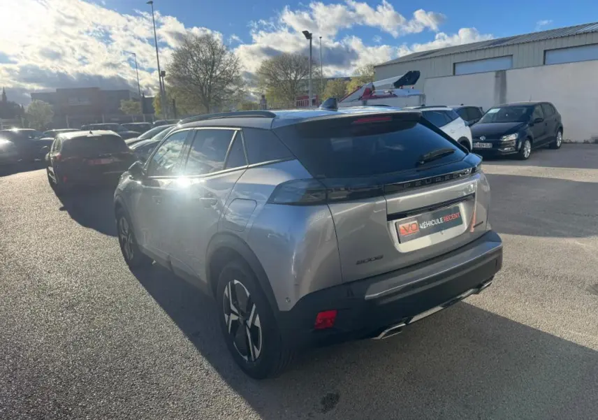 Vue 3/4 arrière droite d’un Peugeot 2008 Hybrid gris avec barres de toit et jantes alliage 17 pouces, stationné en extérieur.