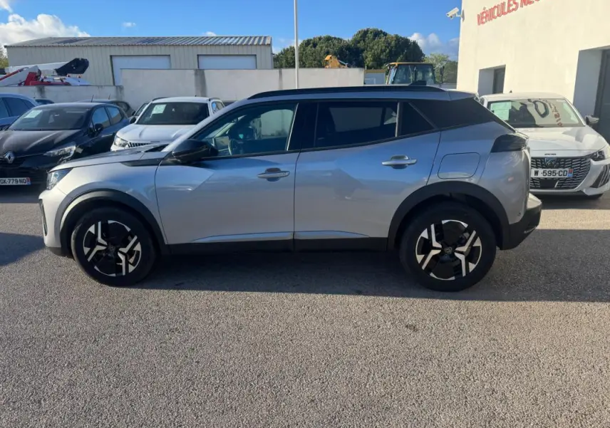 Vue de profil côté gauche d’un Peugeot 2008 Hybrid gris 2024 avec jantes alliage 17 pouces et barres de toit noires.