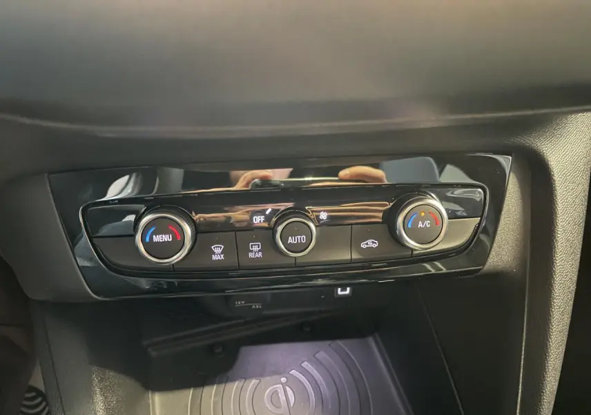 Détail de la console centrale noire avec commandes de climatisation et chargeur smartphone à induction dans Opel Corsa blanche.