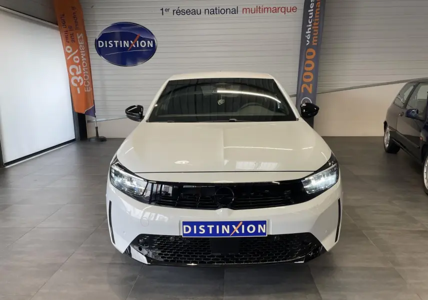 Vue frontale d'une Opel Corsa blanche avec calandre noire et phares LED allumés en intérieur showroom.