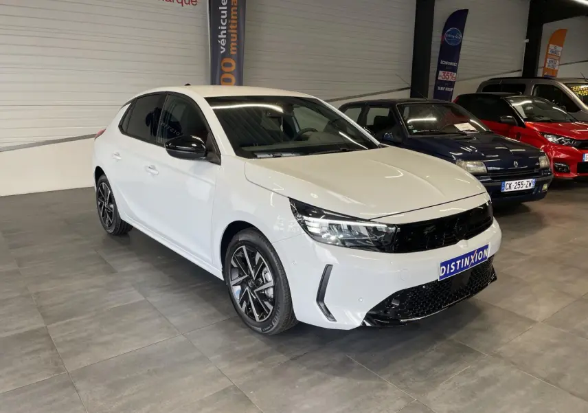 Opel Corsa blanche vue 3/4 avant droit en intérieur, avec calandre noire et jantes alliage diamantées.