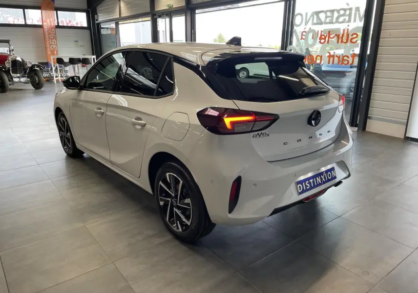 Vue 3/4 arrière droite d'une Opel Corsa blanche avec feux LED allumés et jantes alliage diamantées en showroom.