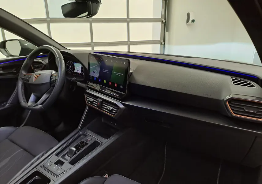 Vue intérieure côté conducteur du tableau de bord et console centrale du CUPRA Leon 2024 avec éclairage d'ambiance bleu.