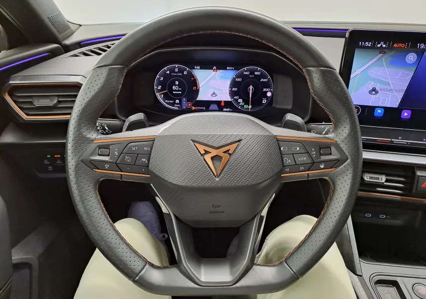 Vue intérieure centrée sur le volant perforé avec logo CUPRA cuivré et tableau de bord numérique lumineux.