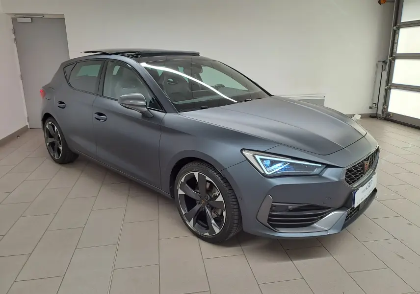 Vue 3/4 avant droite d'une CUPRA Leon 2024 gris magnétique mat avec toit ouvrant panoramique en intérieur.