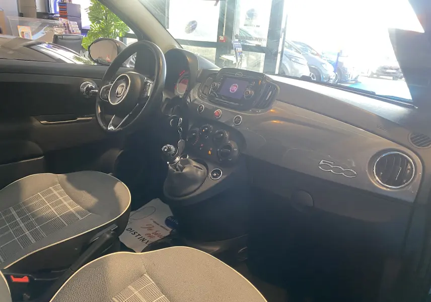 Vue intérieure côté conducteur de la Fiat 500 2019 gris foncé, avec tableau de bord brillant et volant multifonction.