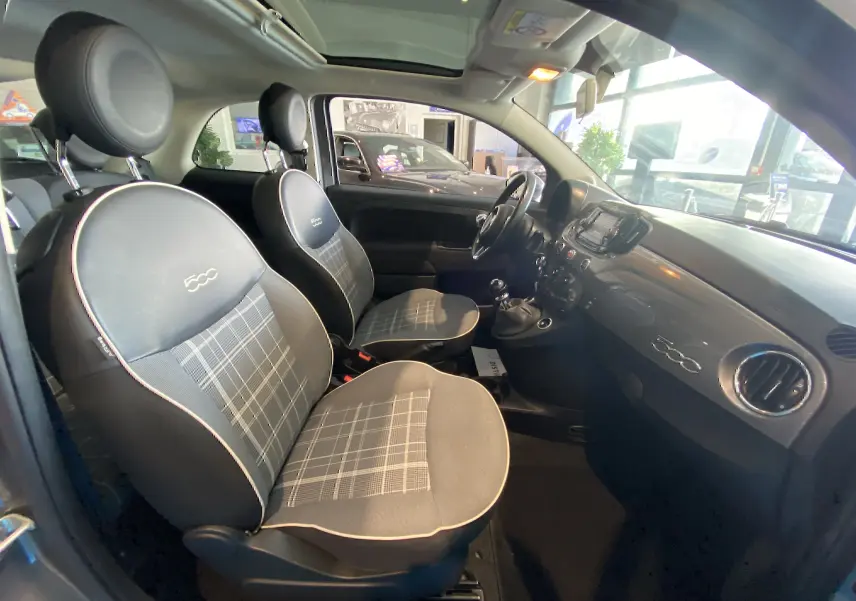 Vue intérieure côté gauche de la FIAT 500 Lounge 2019 avec sièges tissu noir à motif à carreaux et toit panoramique.