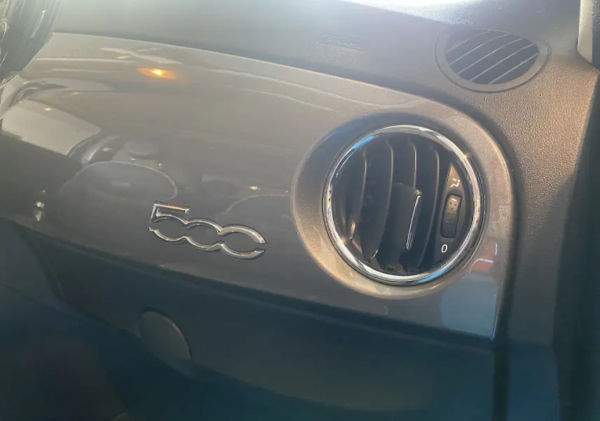 Détail intérieur côté passager du tableau de bord gris foncé avec logo 500 et sortie d’air ronde chromée.