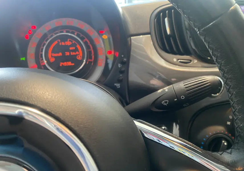 Vue intérieure rapprochée du tableau de bord et volant noir d'une Fiat 500 gris foncé, avec compteur digital allumé.