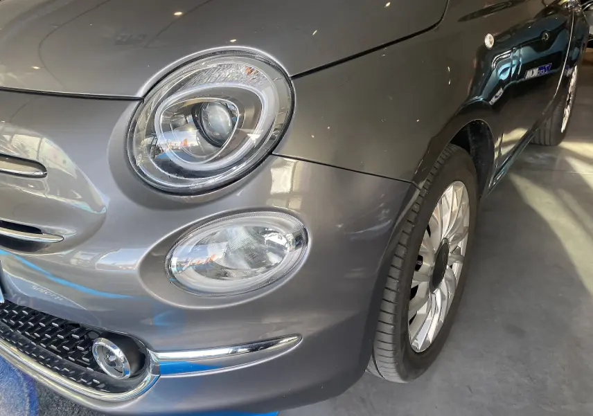Gros plan sur l'avant droit gris foncé du Fiat 500 1.2 8V Lounge, mettant en valeur ses phares ronds et sa roue.
