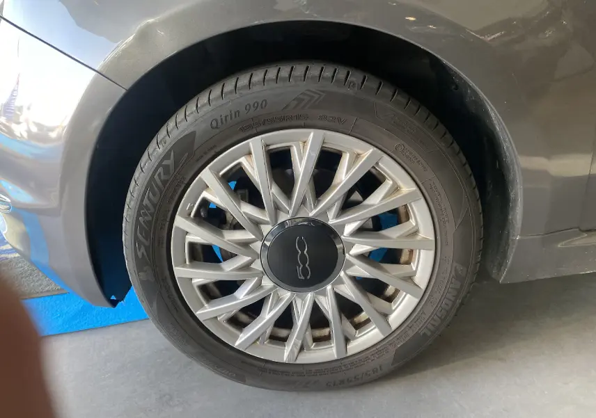 Gros plan sur la roue avant droite d'une FIAT 500 gris foncé, avec jante argentée à rayons fins et logo central noir.