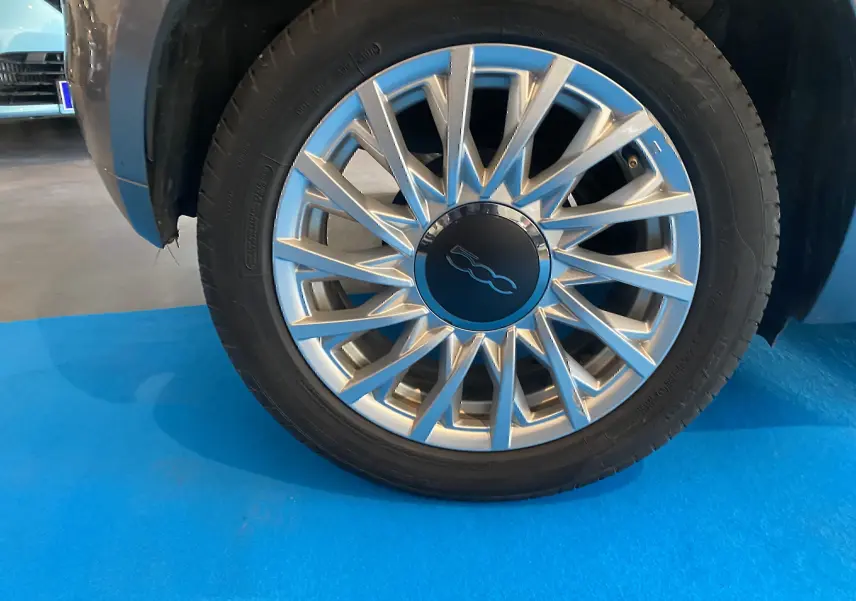 Gros plan sur la roue avant gauche d'une FIAT 500 gris foncé, jante en alliage argentée avec logo central noir.