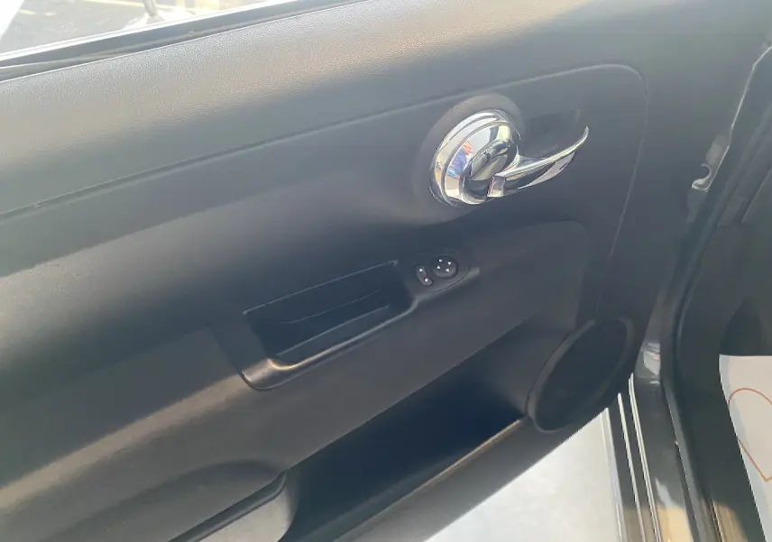 Gros plan sur la porte intérieure côté gauche d'une FIAT 500 gris foncé, avec poignée chromée et commandes de vitres.