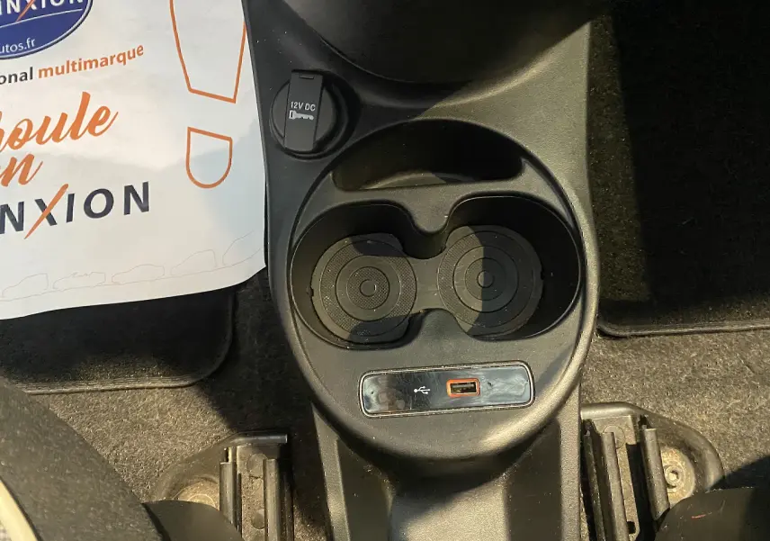 Gros plan sur la console centrale noire de la Fiat 500 gris foncé, avec porte-gobelets et prise USB visible.