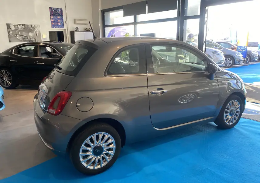 Vue 3/4 arrière droite d'une Fiat 500 Lounge gris foncé, stationnée en intérieur sur sol bleu.