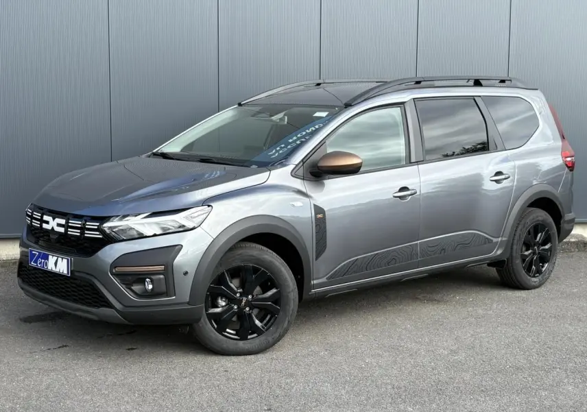 Vue 3/4 avant droit du Dacia Jogger Gris Schiste avec jantes noires et barres de toit modulaires.