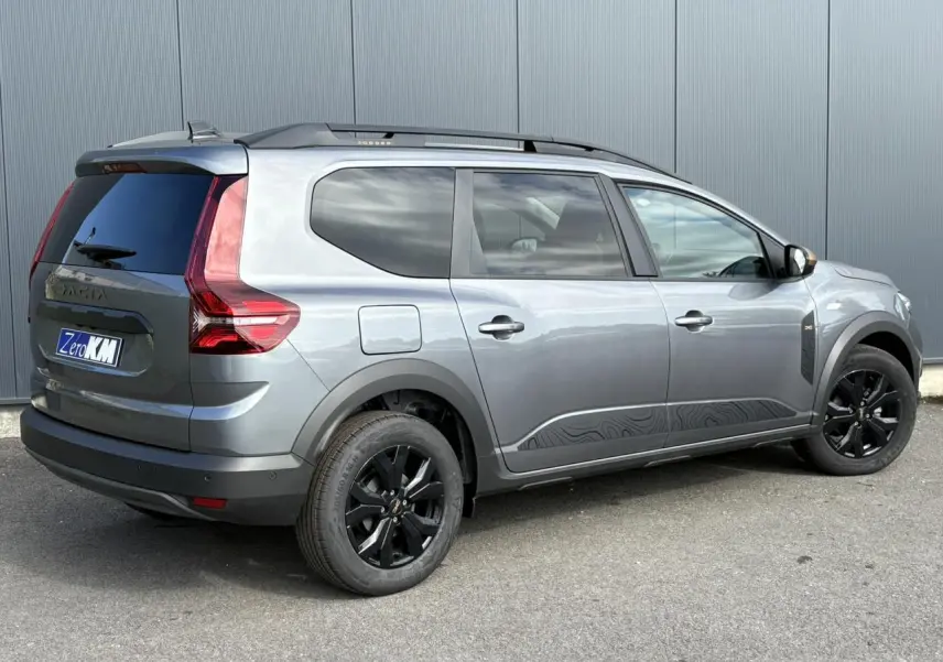 Vue 3/4 arrière droite d'un Dacia Jogger gris schiste avec jantes noires et barres de toit modulaires.