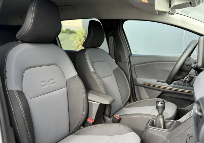 Intérieur du Dacia Jogger 2024 vu côté droit, sièges gris avec surpiqûres et accoudoir central, volant et levier de vitesses visibles.