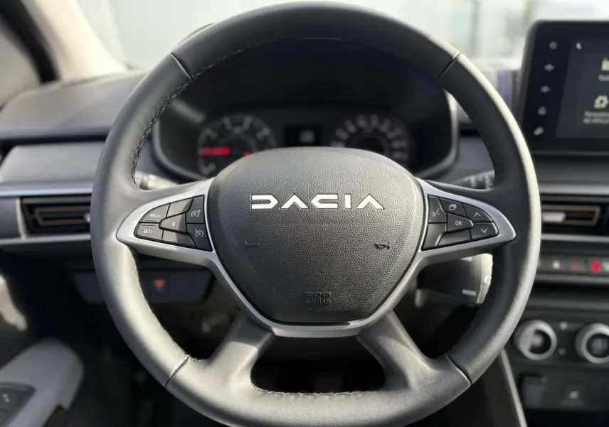 Volant en cuir noir avec commandes intégrées du Dacia Jogger 2024, tableau de bord et écran tactile en arrière-plan.