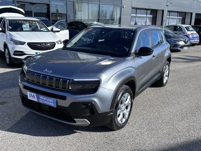 Jeep Avenger gris métallisé en 3/4 avant droit, avec calandre noire distinctive et toit noir contrasté.