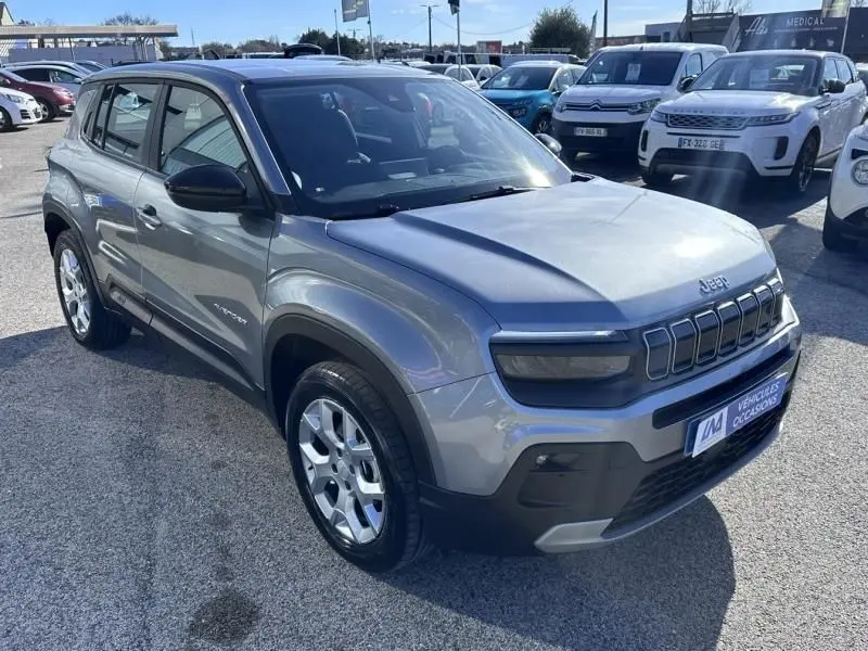 Jeep Avenger gris métallisé en 3/4 avant droit, avec calandre distinctive et jantes argentées visibles.