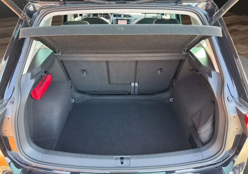 Coffre ouvert vu de l'arrière d'un Volkswagen Tiguan noir intense avec tapis noir et rangement latéral rouge.