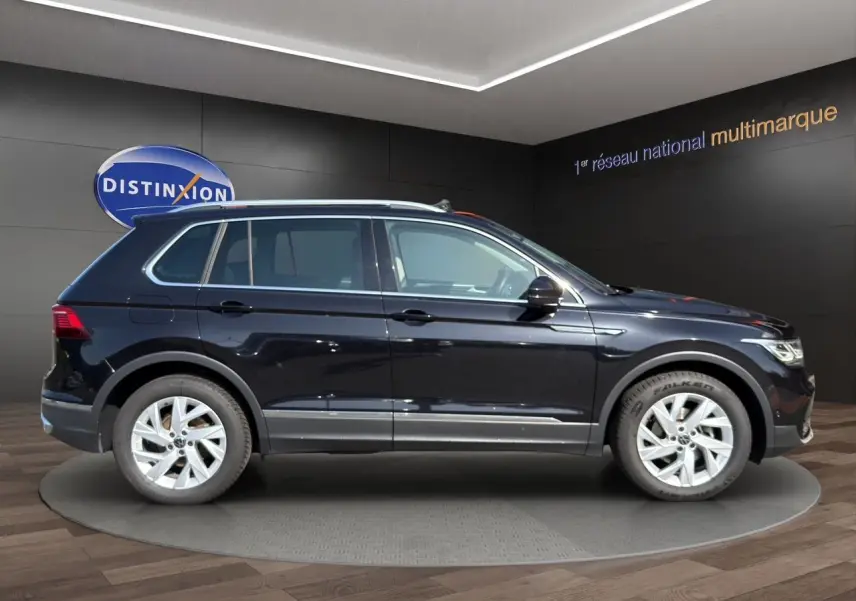 Profil côté gauche du Volkswagen Tiguan noir intense 2022 avec jantes alu 18 pouces dans un showroom.