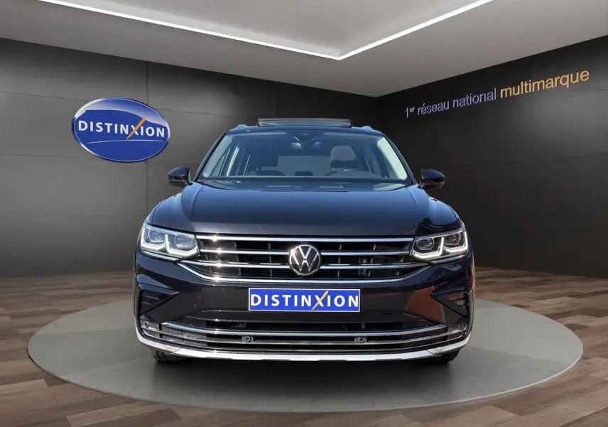 Vue avant du Volkswagen Tiguan noir intense avec calandre chromée et phares LED allumés en showroom.