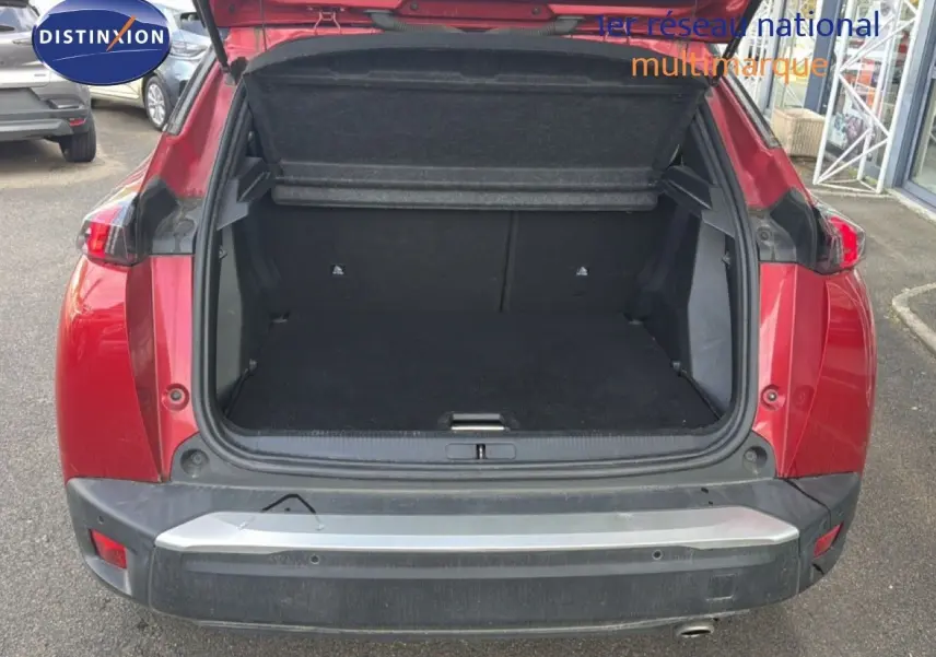 Coffre ouvert vu de l'arrière d'un Peugeot 2008 rouge avec toit noir, montrant l'espace de chargement vide.