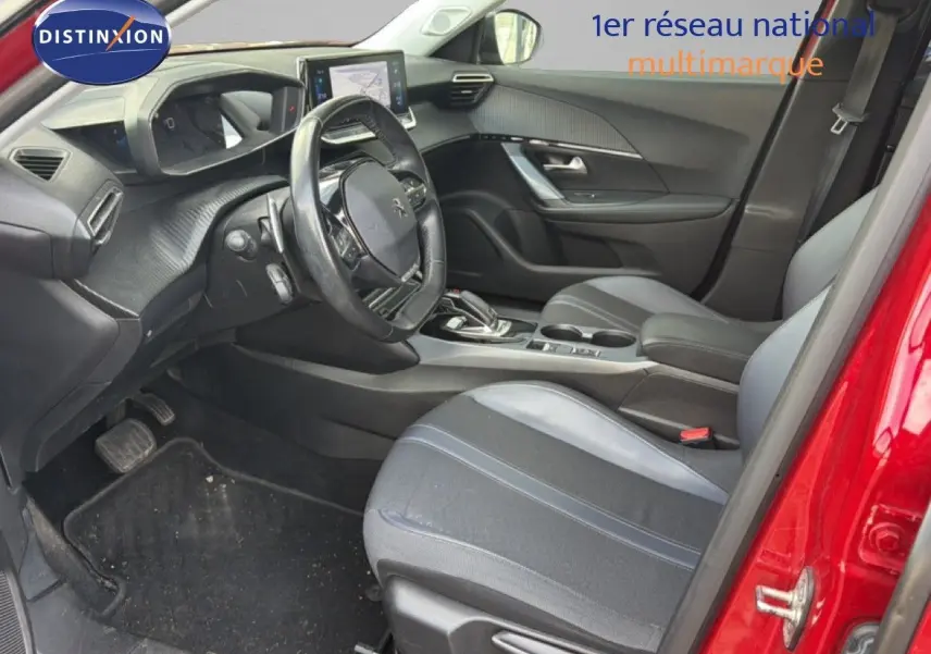 Vue intérieure côté conducteur d'un Peugeot 2008 rouge, montrant le volant, tableau de bord et sièges noirs.