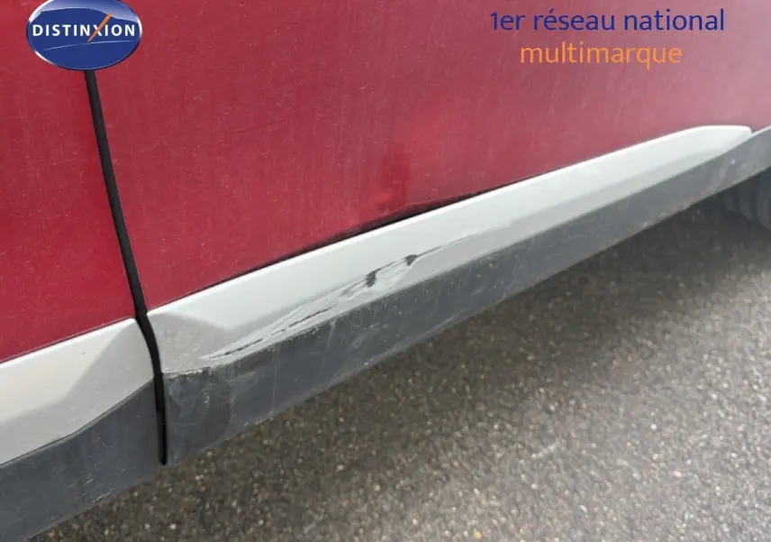 Gros plan sur la partie basse côté gauche d’une Peugeot 2008 rouge avec toit noir, montrant une rayure sur le bas de caisse.