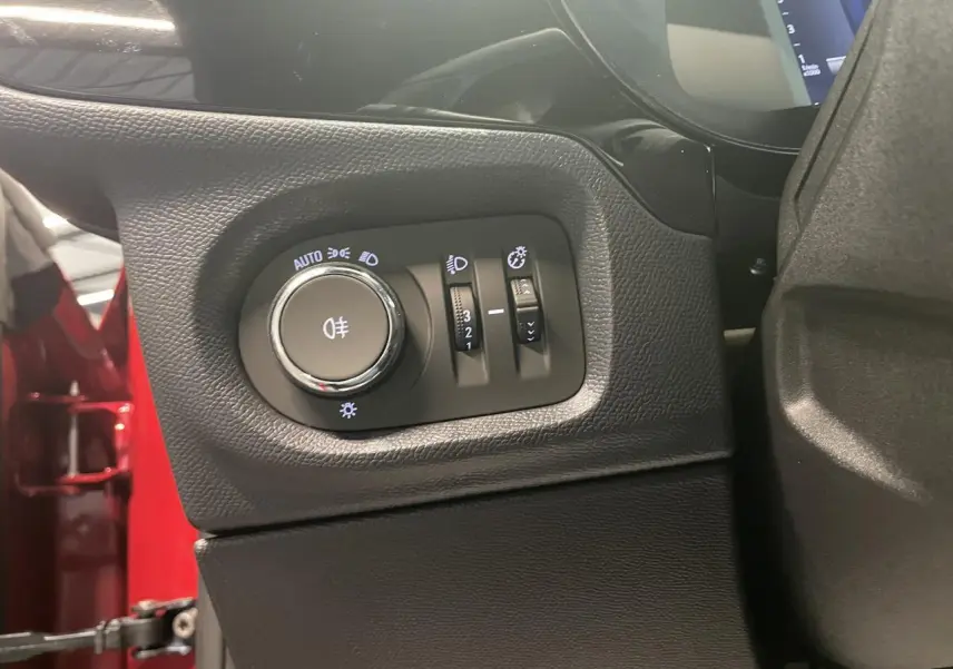 Gros plan sur les commandes d’éclairage à gauche du tableau de bord d’une Opel Corsa rouge, intérieur noir.