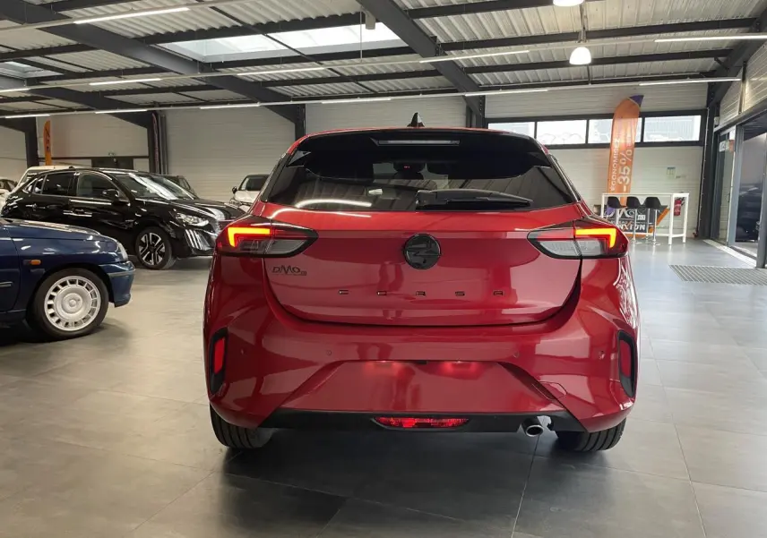 Vue arrière d'une Opel Corsa rouge métallisée avec feux LED et logo noir dans un showroom.