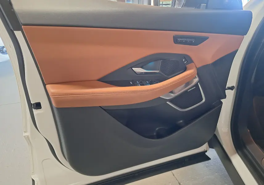 Vue rapprochée de la porte avant gauche blanche du Jaguar E-PACE avec garniture cuir marron et haut-parleur Meridian intégré.