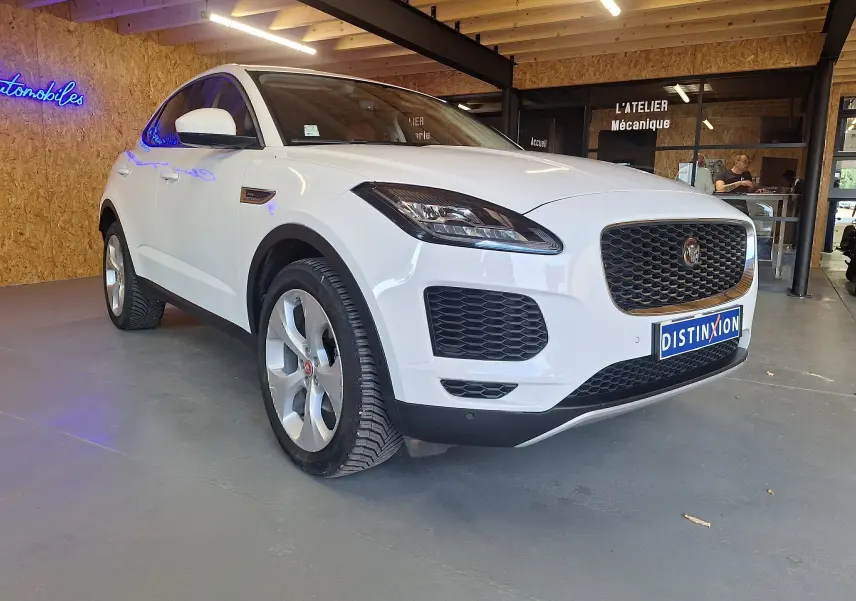 Jaguar E-PACE blanc vue 3/4 avant droit, avec calandre noire et phares LED dans un showroom.