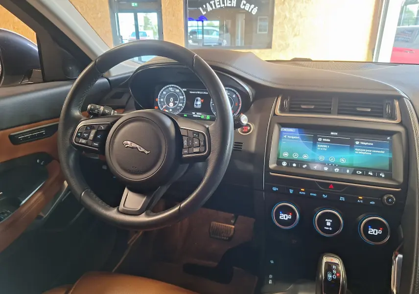 Intérieur du Jaguar E-PACE blanc 2019, vue du poste de conduite avec volant cuir et écran tactile central.
