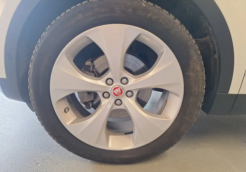 Gros plan sur la roue avant droite argentée avec logo Jaguar rouge sur un SUV blanc Jaguar E-PACE 2019.