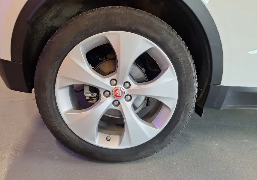 Gros plan sur la roue avant droite du Jaguar E-PACE blanc, avec jante argentée et logo Jaguar rouge au centre.