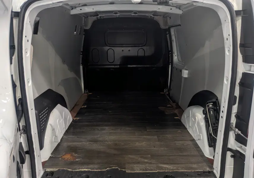 Vue intérieure arrière du Renault Kangoo Express blanc minéral, montrant l'espace de chargement vide avec plancher en bois usé.
